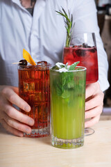 Alcoholic cocktails with ice in glasses on the bar table and bartender's hands