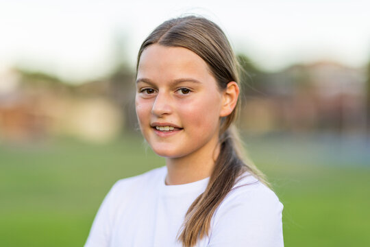 head and shoulders of one pre-teen girl outdoors with long hair tied back and wearing white tee
