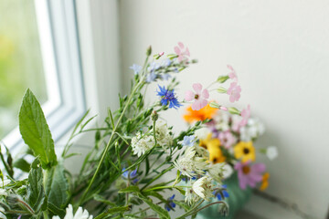 Stylish colorful wildflowers bouquet on tile shelf on rustic wall background. Beautiful summer flowers in vase gathered from garden, floral arrangement at window in home