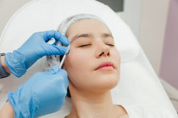 Close-up of the hands of a beautician injecting Botox into a woman's forehead. Correction of forehead and eye wrinkles with botulinum toxin.