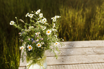 Beautiful wildflowers bouquet in sunlight on rustic wooden table in garden among grass. Beautiful summer flowers in vase gathered from garden, arrangement in countryside home. Copy space