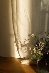 Stylish wildflowers bouquet in evening sunlight against window in rustic room. Beautiful summer flowers in vase gathered from garden, floral arrangement in countryside home