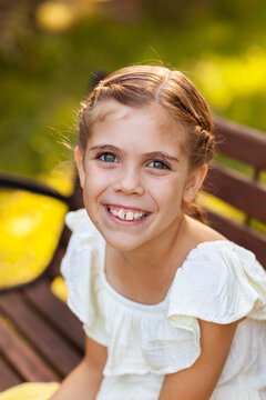 Happy nine year old girl in yellow dress sitting on park bench
