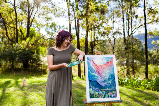 Young nineteen year old artist hobbyist with her painting standing outside in clearing