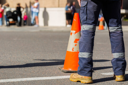 Worker with high vis standing near traffic cone on road closed for parade