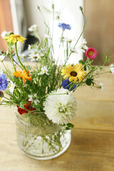 Stylish wildflowers bouquet in sunlight on rustic wooden table. Beautiful summer flowers in vase...
