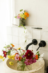 Beautiful flowers in modern bathroom with stylish sink, black faucet and white tiles. Summer flowers arrangement gathered from garden in modern room in home