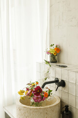 Beautiful flowers in modern bathroom with stylish sink, black faucet and white tiles. Summer flowers arrangement gathered from garden in modern room in home