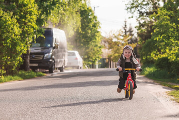 A cheerful little boy rides a bicycle outdoors. A happy child walks in the spring park. The baby is dressed in a fashionable vest, overalls. An aviator's hat is on his head.