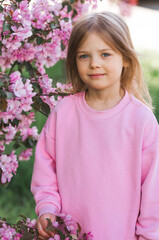 Spring flowering. Portrait of a beautiful little girl 4 years old in a pink blouse in nature against a background of pink flowering apple trees. Childhood. The baby is posing.