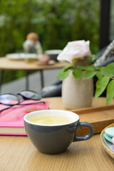 A cup of green tea on a wooden table with a notebook and glasses on a green background