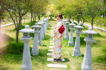 Young woman wearing a Japanese traditional kimono or yukata stand in a garden with torii poles.