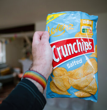 Paris, France - May 2, 2023: A mans hand holds a bag of Lorenz Salted Crunchips, ready to enjoy their salty snack goodness living room background