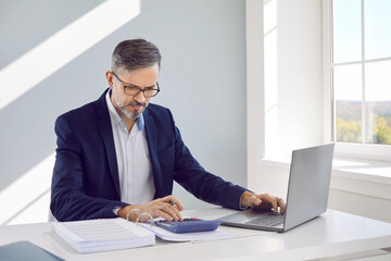 Businessman sitting at laptop computer calculating expenses. Focused middle aged man accountant, financial adviser wearing glasses expendituring pay bills. Accounting, statistics, analytical research