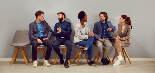Office multiracial people in casual wear resting in restroom. Two groups of colleagues communicate while sitting on comfortable ergonomic chairs. Waiting in hallway at bosss office.