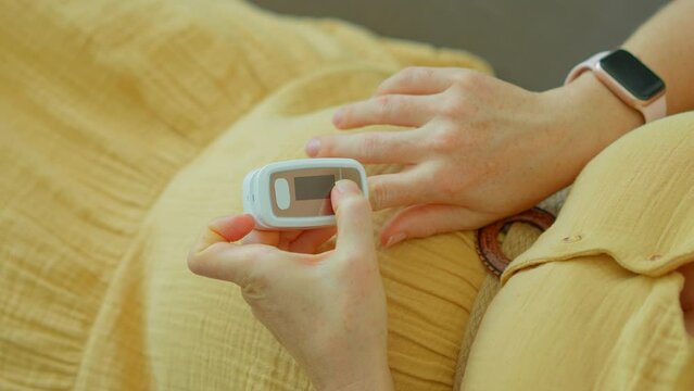In this video, a pregnant woman is seen measuring her oxygen levels using a pulse oximeter. The slow motion footage captures the device being placed on her finger and displaying the reading.