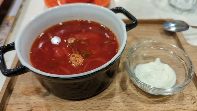 Borsch soup in a black plate and sour cream on a wooden tray
