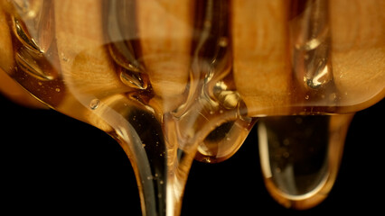 Honey dripping, pouring from wooden dipper close up on black background. Healthy organic honey