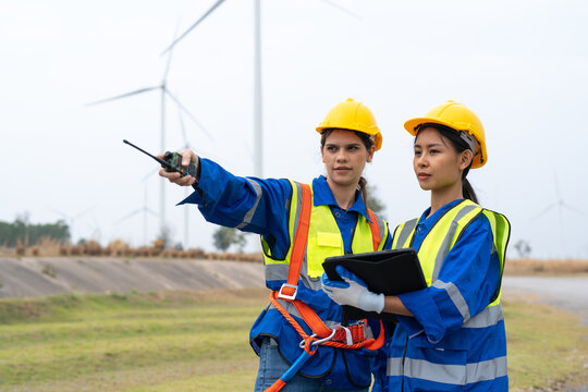 Female engineer in uniform with helmet safety pointing and holding tablet inspection and maintenance of wind turbine in wind farms to generate electrical energy, Renewable power energy.