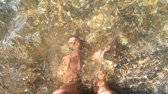 Woman standing with her bare feet on the sandy rocky bottom of the sea and digging her feet into the sand. Bare foot woman caucasian in transparent water closeup. Relax travel rest tourism vacation