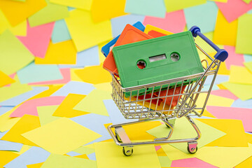 an shopping cart with vintage retro audio tape cassettes on a background of multicolored paper sticky notes
