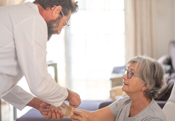 Fototapeta premium Physiotherapist visiting a senior patient with right thumb osteoarthritis helping her to put on a thumb splint. Pain and rehabilitation of the elderly woman