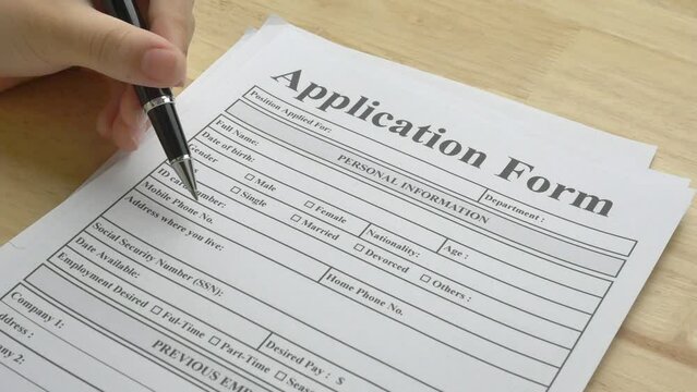 A woman's hand holds a black pen and points at an application form, reading the details titles before filling in the information. The concepts of job employment, human resources, business recruitment.