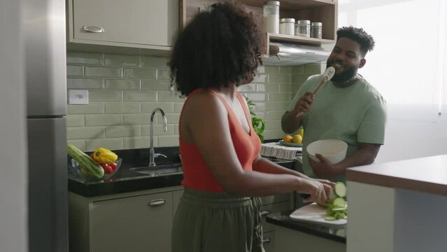Happy joyful black couple husband and wife having fun singing in the kitchen, cooking together at home. Overjoyed young couple in love preparing meal healthy food, enjoying active family weekend
