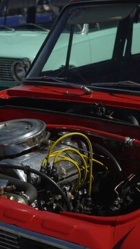 Old car without hood stands on open air site in retro car restoration workshop. Clean shiny carbureted engine with new wires and fuel rail with polished shiny air intake, vertical video.