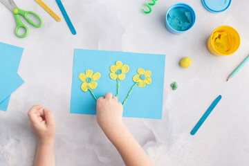 Blue and yellow flowers from plasticine. Kid's craft. Child's hands with dough clay. Colorful clay