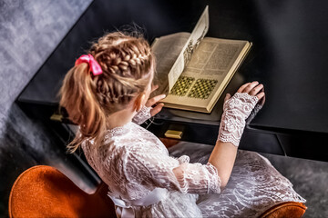 A little blonde girl is reading a book at the table. Studying at home, doing homework. The concept is coming to school soon