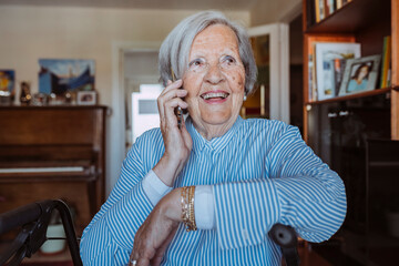 Happy old grandmother on the phone, sitting in walker wheelchair at home, looking away. Elderly...