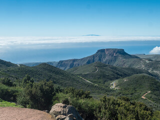 Scenic view on table mountain Fortaleza seen from peak of Alto de at Garajonay mountain. White clouds and El Hiero island above, blue sky. La Gomera, Canary Islands, Spain.