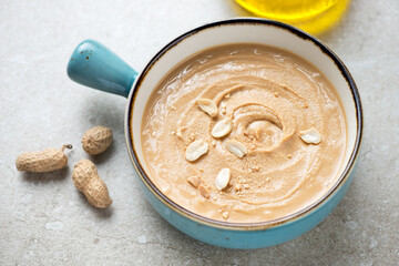 Turquoise serving bowl with peanut butter or a paste made from ground, dry-roasted peanuts, horizontal shot on a beige stone background