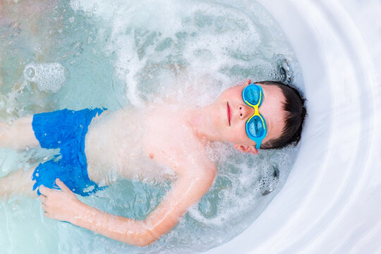 Serious boy in swimming goggles bathing in hot tub