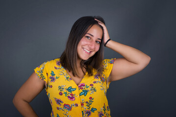 Shot of happy young woman with positive smile, has long hair, rejoices having weekend and good rest after hard working exhausting week, isolated on gray wall.