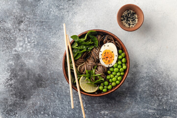 Asian soba noodle soup, with chicken, boiled egg, sesame seeds, green pea and green onion served with chopsticks. Top view, flat lay, text space