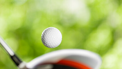 Golf club hitting ball on grass against blur background