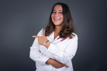 Young beautiful doctor woman wearing medical uniform coat and stethoscope standing over white studio background. 