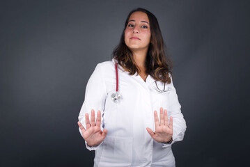 Beautiful brunette girl over isolated background afraid and terrified with fear, and disgusted expression stop gesture with both hands saying: Stay there. Panic concept