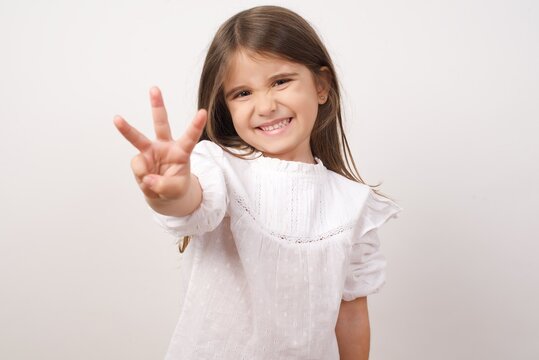 Cute charming little girl wearing white shirt over white background pointing up with fingers number three, third, 