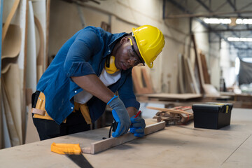 Male carpenter measure the size of wood during working in wood workshop. Male joiner wearing safety uniform, gloves, helmet and working in furniture workshop