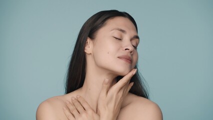 An attractive young woman runs her fingers across her face, gently touching smooth, healthy skin....