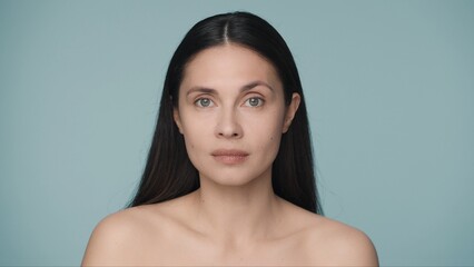 Close up portrait of a seminude woman on a blue background. A woman with natural make up looks straight ahead. Beauty concept. Natural beauty, cosmetology, skin care.