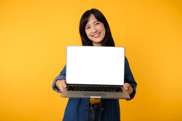 Naklejka premium portrait young happy woman wearing yellow t-shirt and denim shirt holding laptop and point finger to screen isolated on yellow studio background. business technology application communication concept.