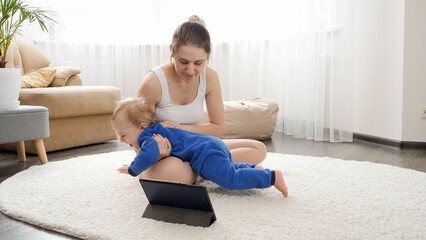 Young mother with baby boy watching online fitness course on tablet computer and doing exercises. Family healthcare, active lifestyle, parenting and child development