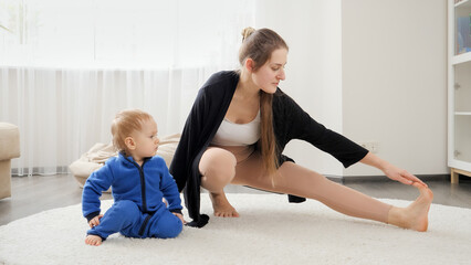 Beautiful young woman with little baby son doing stretching and fitness on carpet at home. Family healthcare, active lifestyle, parenting and child development