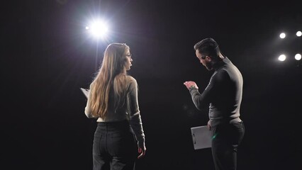 Back view of enthusiastic business coaches in informal wear exchanging their thoughts with audience during conference session. Caucasian male and female using headsets and clipboards on black stage.