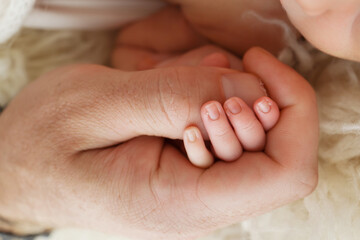 Close-up of a small hand of a child and the hand of mother and father. A newborn baby after birth holds tightly, squeezes the thumb of its parents. 