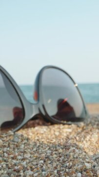 Things on the beach by the sea. Through pink flip flops and sunglasses and a red apple. Dolly Vertical.